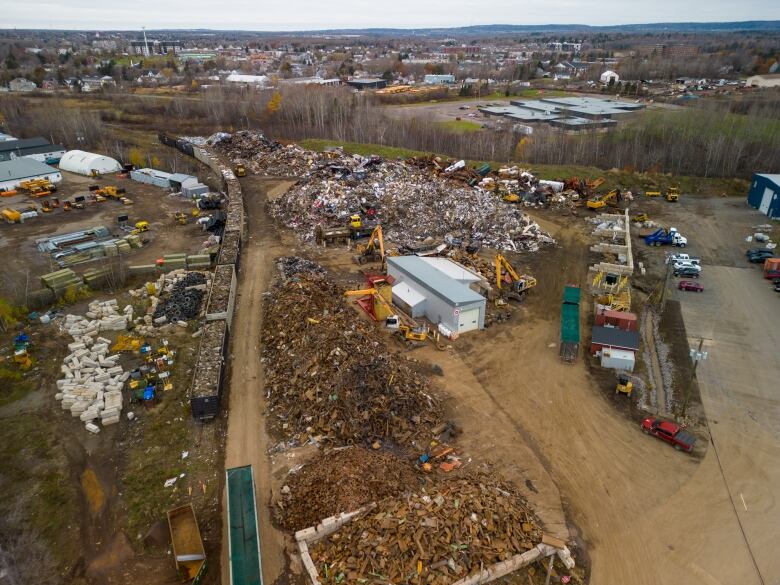 Various piles of crushed metal with a rail line and rail cars on the left side.