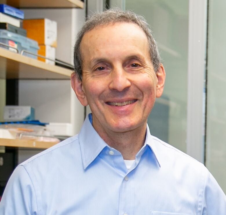 A man in a pale blue shirt smiles for a photo taken in a medical office.