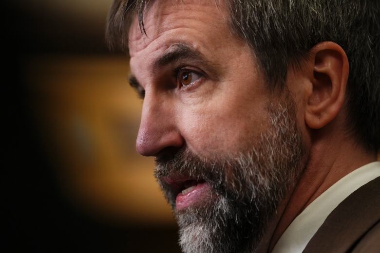 A close up on a man with a beard as he speaks to reporters who are not pictured.