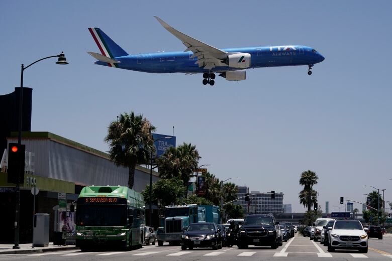 A low-flying plane approaches an airport while it is just above a busy street. 