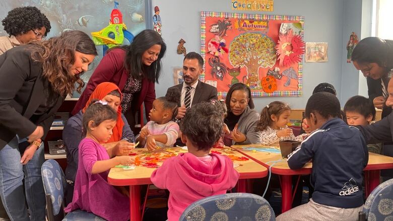 Adults play with children seated at a table at a day care.