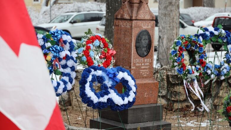 Wreaths and a Canadian flag surround a grave marker with an engraving of a man's face and the words 