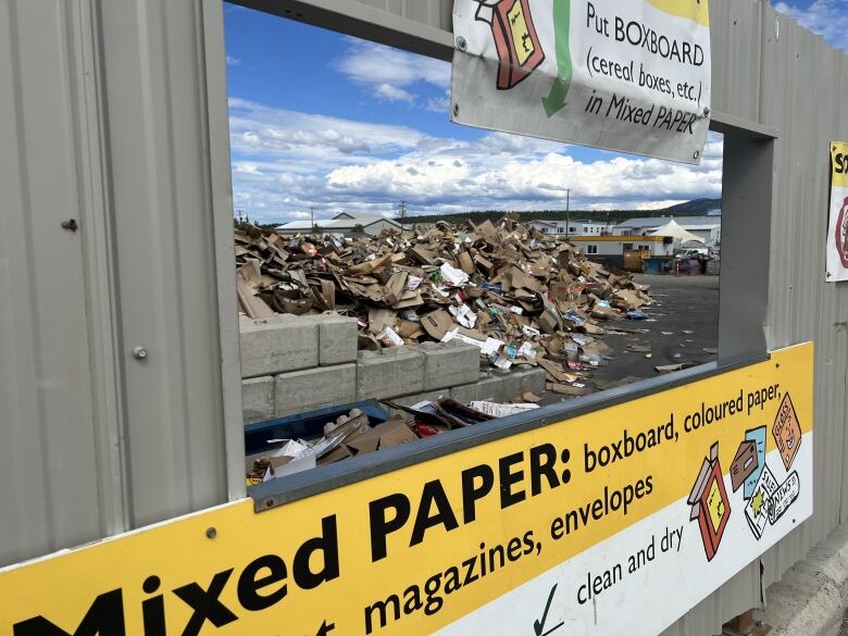 A pile of cardboard is seen through an opening with a sign marked, 'mixed paper.'