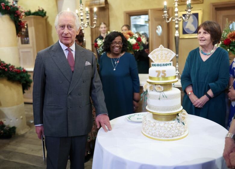 A person stands beside a table with a three-tier cake on it.