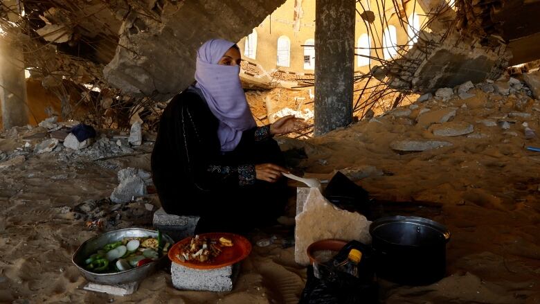 A woman cooks on the ground in a destroyed mosque.