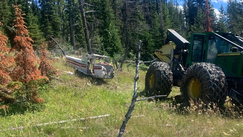 A plane fuselage sits on a grassy mountainside next to a large green tractor