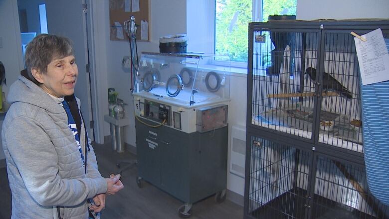 A woman stands by a cage with a crow inside.