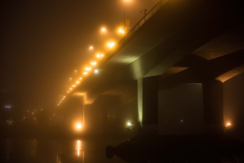 A well-lit street bridge is seen through fog in the nighttime. 