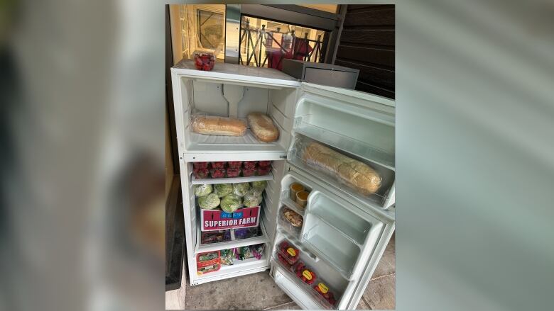 An open fridge is pictured with bread, vegetables including lettuce, and berries.