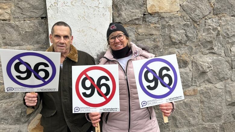 Two people hold up signs showing a crossed out 96.