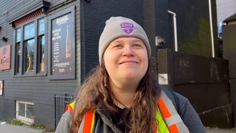 A woman wearing a safety vest and a SIEU toque smiles at the camera