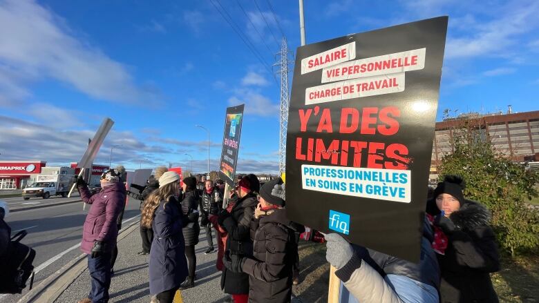 A group of people hold French-language signs outdoors on a sunny day.