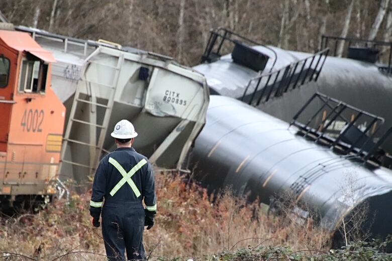 A man wearing a hard hat stares at a derailed train.