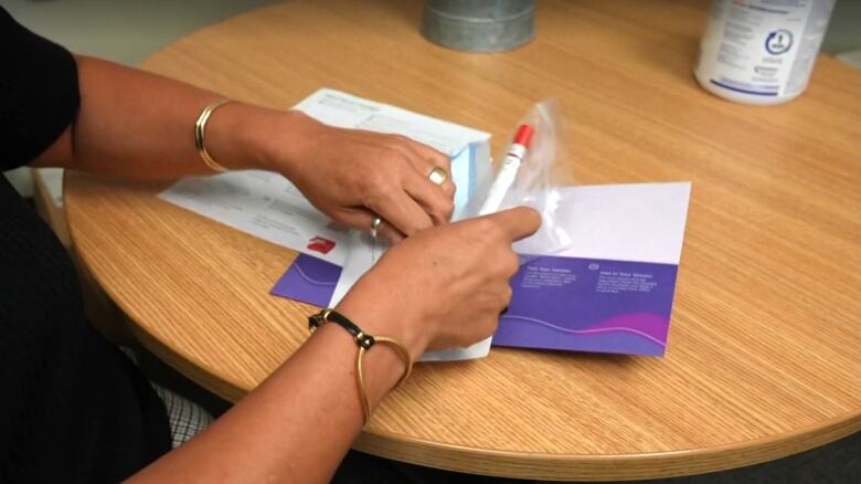 A person's hands are seen holding a collection tube and putting it into an envelope. 