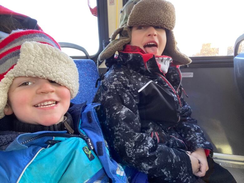 Two young boys dressed in winter wear make goofy smiles as they ride the bus.