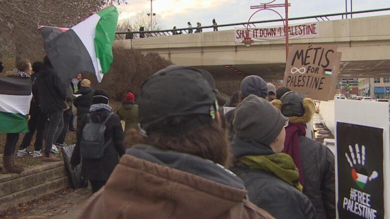 A group of protesters are pictured. Two hold signs which say, 