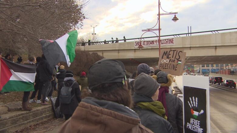 A group of protesters are pictured. Two hold signs which say, 