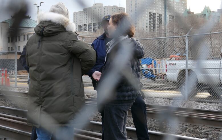 Two people are pictured speaking in a circle with two police officers on a rail line.