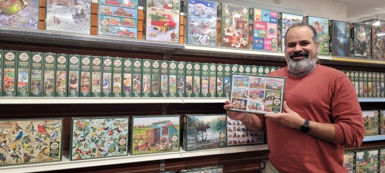 A man holds a puzzle in front of a display of puzzles.