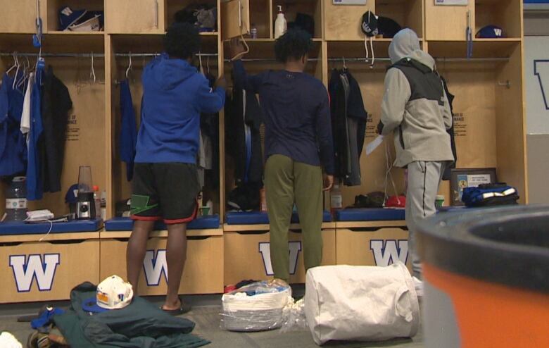 Three people clean out lockers in a football locker room.