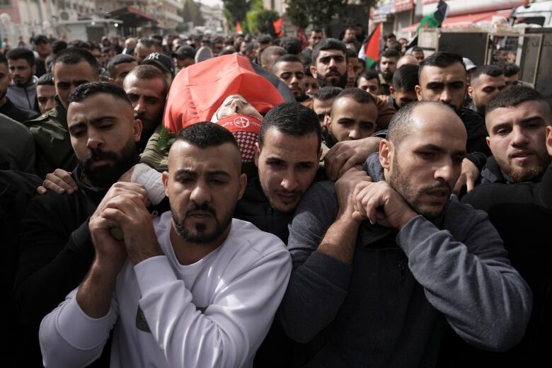 A crowd carries the body of a deceased man wrapped in cloth.