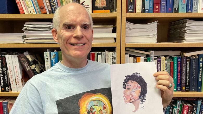 A man in front of a bookcase holds a medical anatomy illustration. 