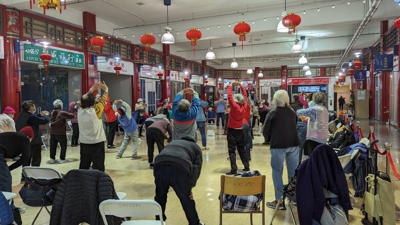 A group of seniors are stretching in the centre of a mall. 