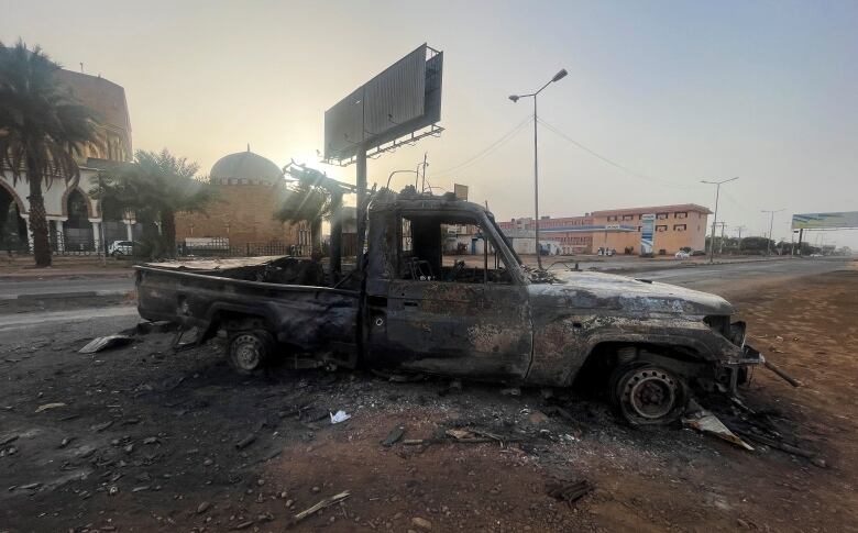 A burned vehicle sits on the side of the road.