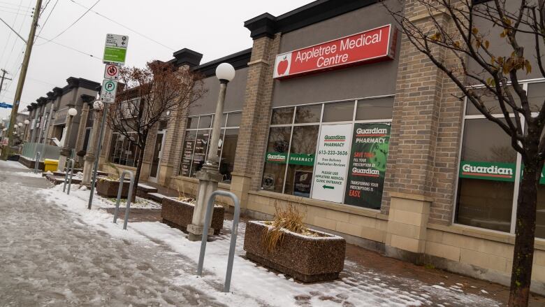 A one-storey business building on a city street. There's snow on the ground and a sign for a medical clinic on the window.