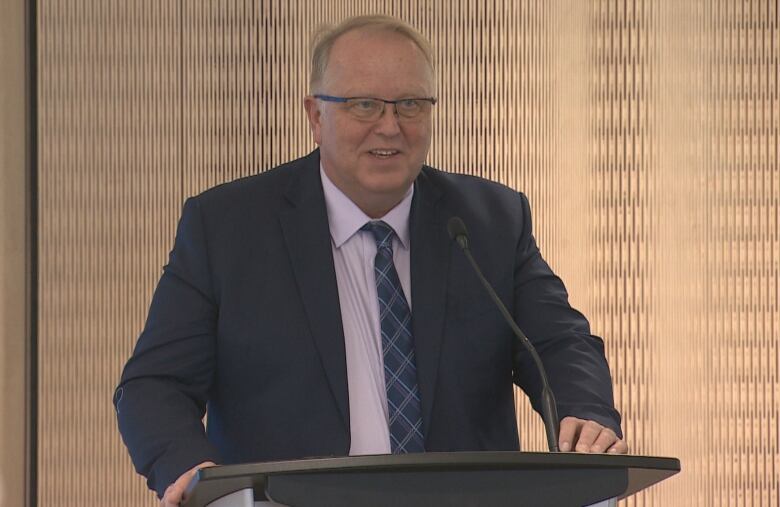 A man with glasses stands at a podium.