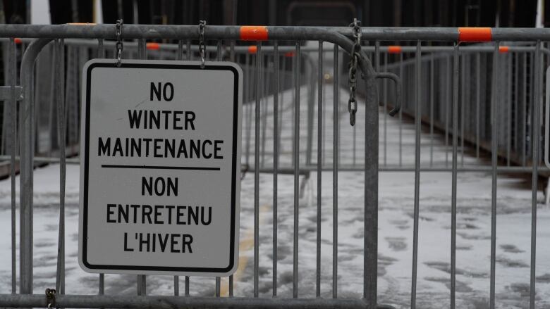 A sign on a fence blocking a bridge says 'no winter maintenance'