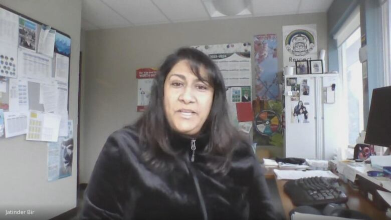 A South Asian woman speaks in an office filled with equipment and charts on the wall.