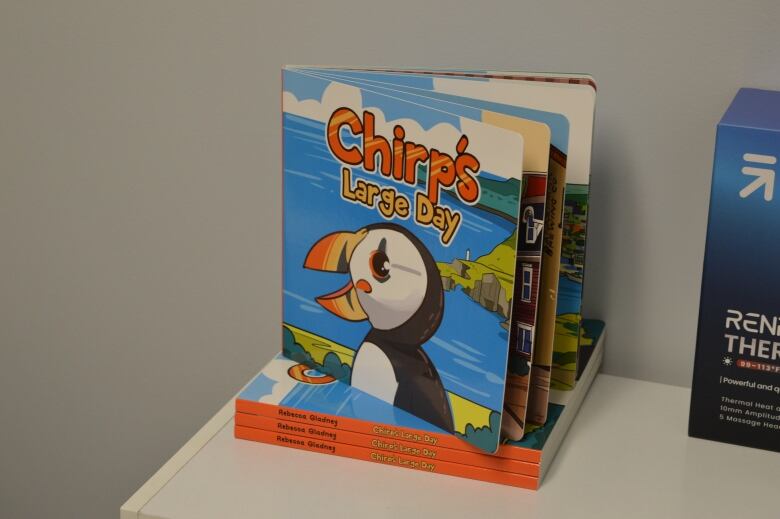 A children's book with a cartoon puffin on the cover called Chirp's Large Day sits on top of a white shelf. 