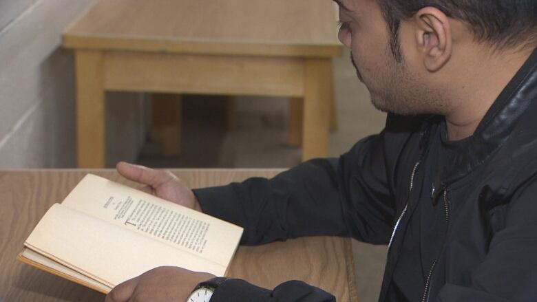 A man in a black jacket sits at a table with a book open in front of him.