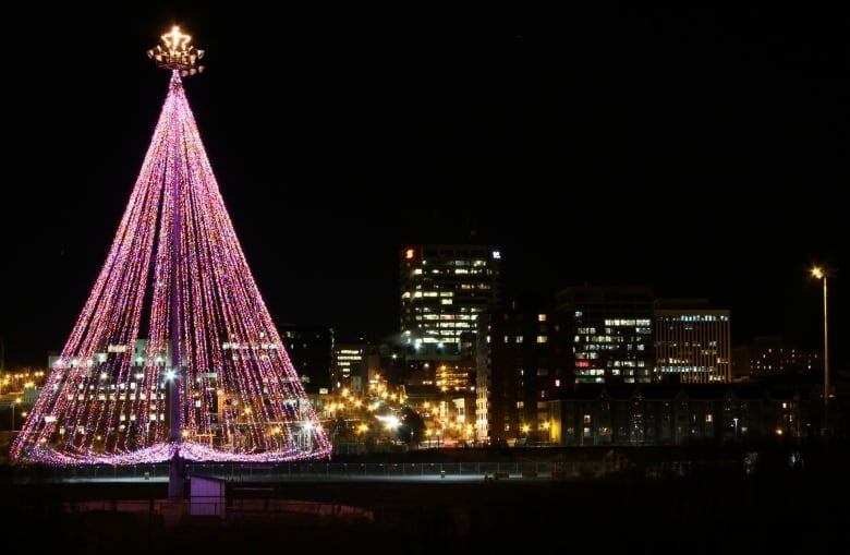 Christmas tree with strings of twinkle lights in front of a cityscape.