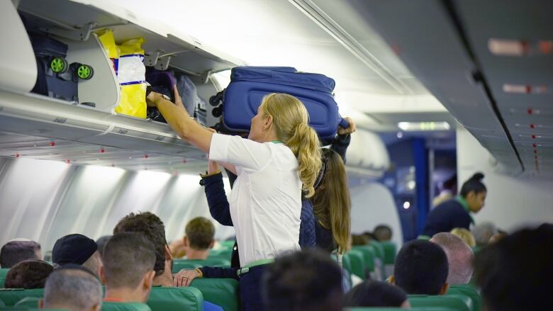 A flight attendant helps the passengers to put their luggage in the cabin of the plane. 