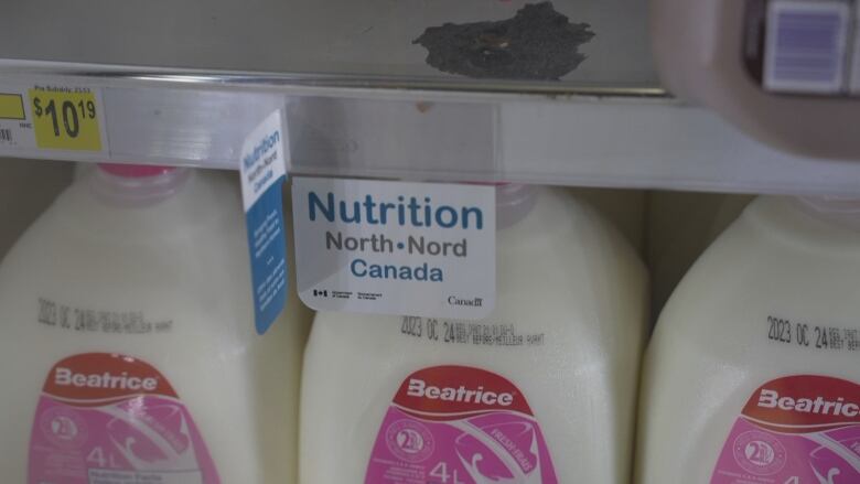 Milk sits in a grocery store display fridge. A sign on the shelf says 