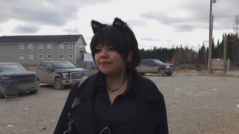 A woman stands on a gravel parking lot.