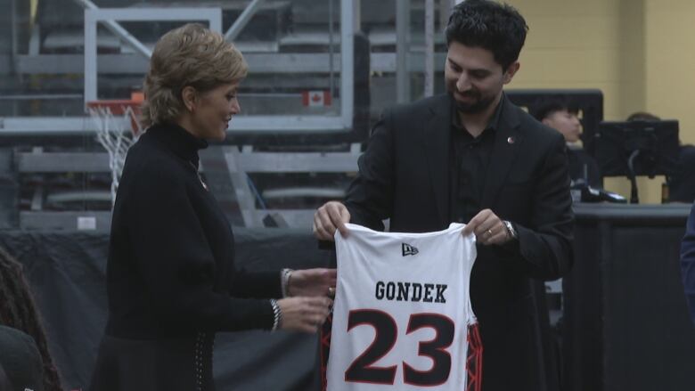 A man hands a basketball jersey to a woman.