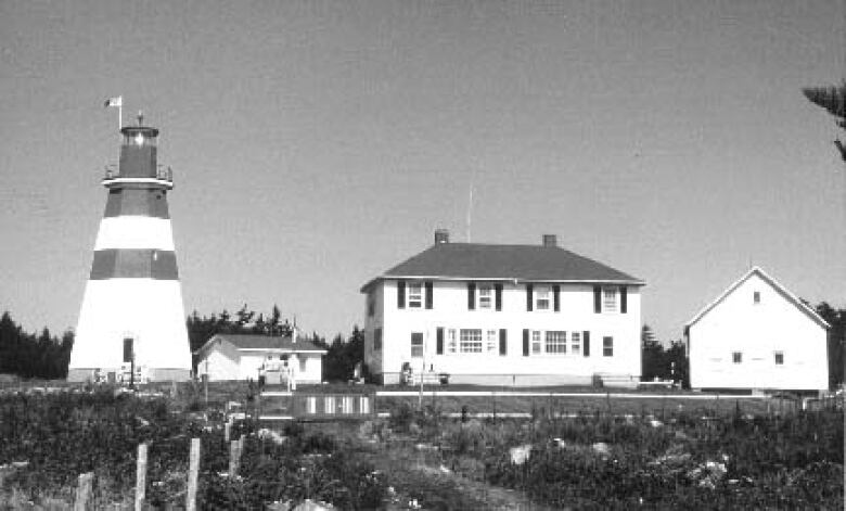 A black and white photograph of a lighthouse and three nearby buildings