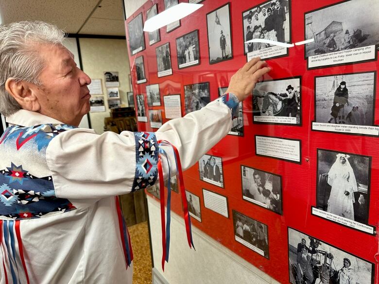 Man points to black and white photos of his family on a display wall at the museum.