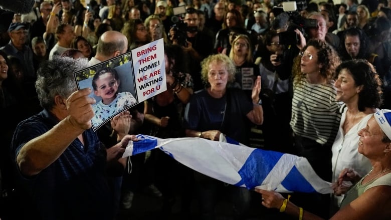 Several people are shown at a nighttime gathering outside, some holding signs and waving flags.