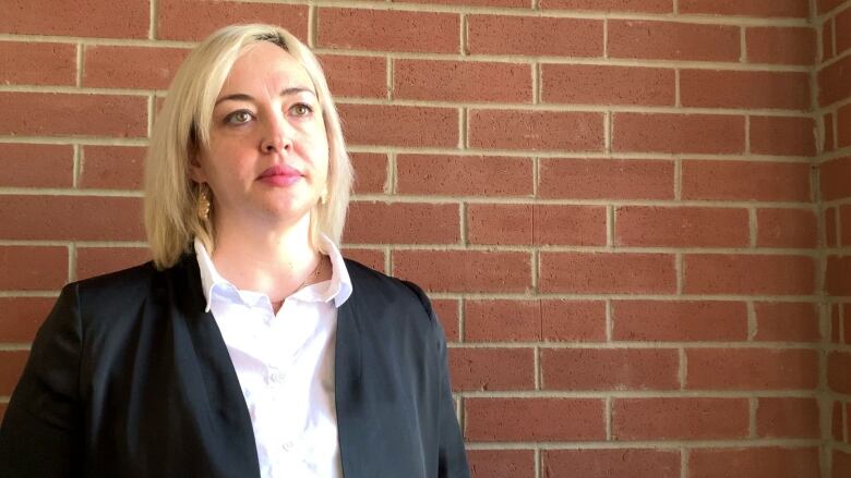 A woman wearing a black jacket is pictured in front of a brick wall.