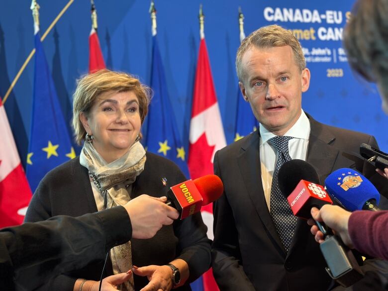 Two people standing in front of reporters arms holding microphones.