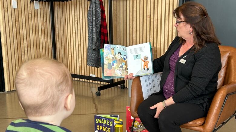 A young child sits and looks at a woman reading aloud from a book.