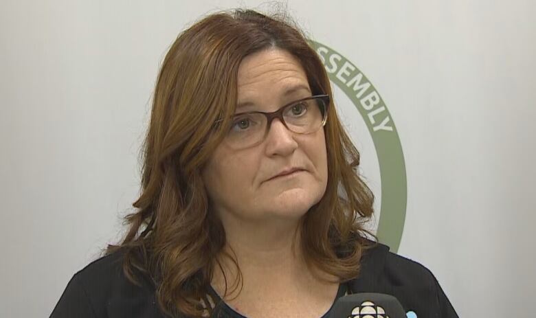 A woman stands in front of a microphone waiting to answer questions from reporters.