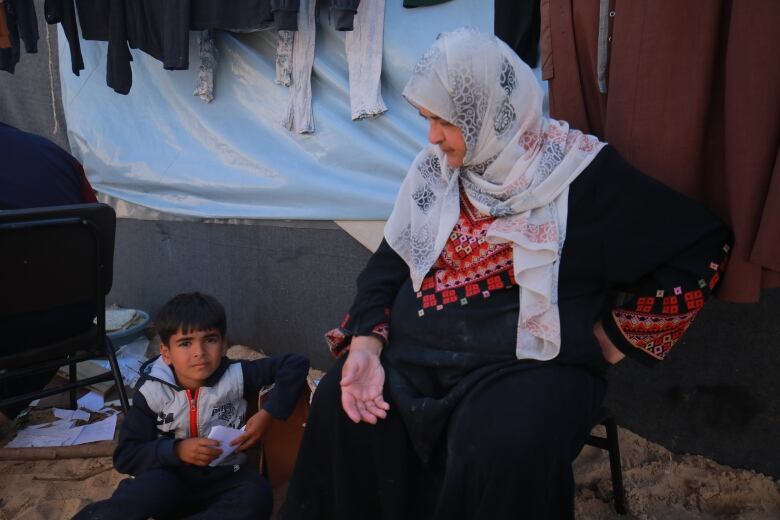 A woman and a child sit outside a tent.