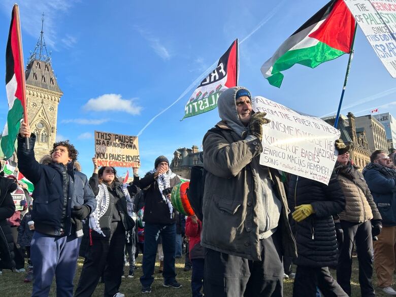 A man holds a sign at a protest, while other people hold Palestinian flags. 