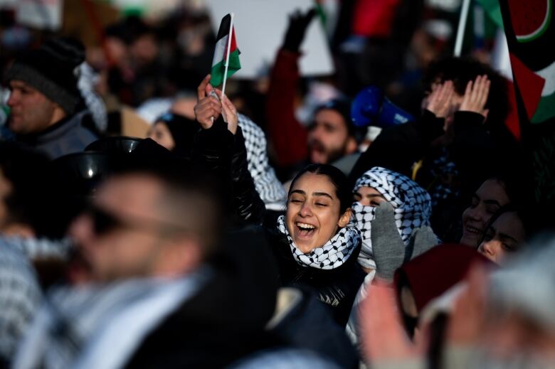 A woman chants and holds a flag while being surrounded by many other protesters.