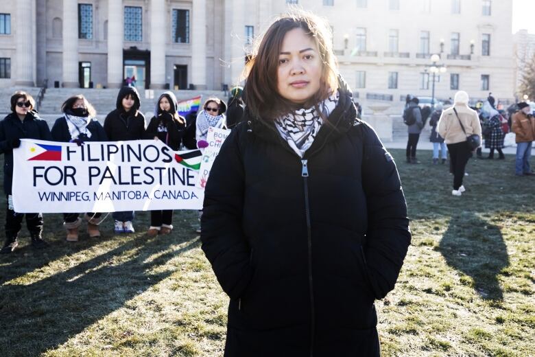 A woman in a black jacket stands in front of a 'Filipinos for Palestine' banner.